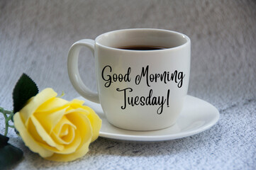 Good morning Tuesday text on coffee cup yellow flower on blurred marble background.