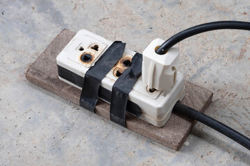 Burnt electrical socket and plug, poor quality product on the cement floor background.