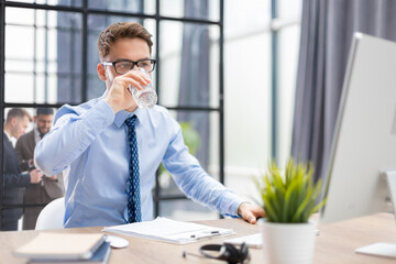 Handsome businessman using PC and drinking water in office area with collegues on the background