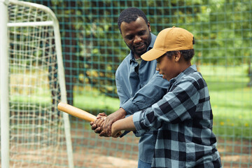 African father teaching his son to hold the bat in right way during their baseball game outdoors
