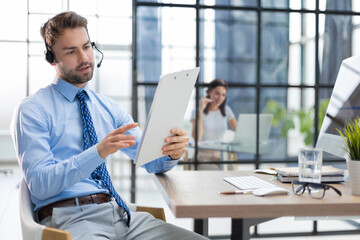 Young man is working with papers while sitting in the office with collegues on the background. Successful entrepreneur is studying documents with attentive and concentrated look