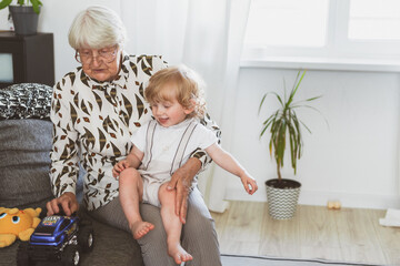 Elderly woman with her little grandson playing at home on the sofa