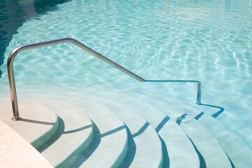 Steps going into aqua blue swimming pool with metal hand rail 