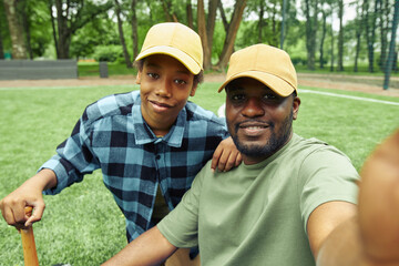 Selfie portrait of happy dad and son in caps during their game in baseball in park outdoors