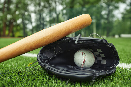 Close-up view of white leather baseball ball and glove with bat on green field for baseball game