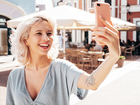 Young beautiful smiling hipster woman in trendy summer dress clothes. Sexy carefree model posing in the street at sunny day. Positive blond female outdoors. Cheerful and happy. Taking selfie photos