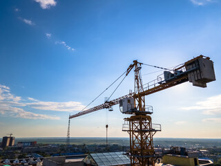 Fototapeta na wymiar Construction crane on the background of a clear day sky aerial view. Flyby of a construction crane on a quadrocopter against the background of an epic blue sky with the sun, close-up
