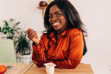 Beautiful young woman eating yogurt in the kitchen in the morning. Healthy food. Close up. Portrait...