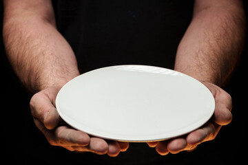 Male hands holding empty plate on dark background, lack of food, hunger concept.