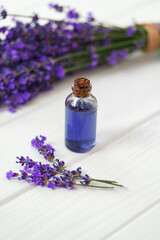 Herbal oil and lavender flowers on white wooden background