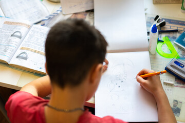The boy at the table draws, does homework, is engaged in creativity. A man holds his head with his hand. a table stands by the window