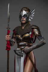 Studio shot of attractive woman warrior dressed in ancient armor holding axe and spear.