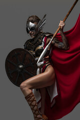 Shot of combative valkyrie from past with shield and spear dressed in armor against grey background.