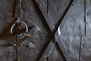 Fragment of an old powerful black iron door. The metal surface is oxidized. There are brutal structural elements and a padlock. Background. Texture.