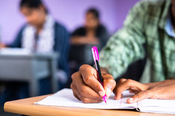 Close up shot of college student writing notes on book at classroom - concept of examination,...