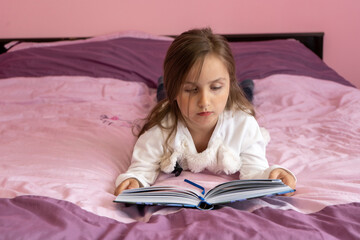 Cute little girl reading a book on the bed