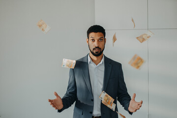 Serious young businessman man standing in officethrowing money away, inflation concept.