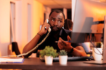 Young businessman talking to people on landline phone, answering call to discuss about research information for report presentation. Chatting on office telephone line to do company paperwork.