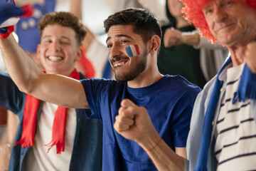 Excited football fans supporting French national team in live soccer match at stadium.