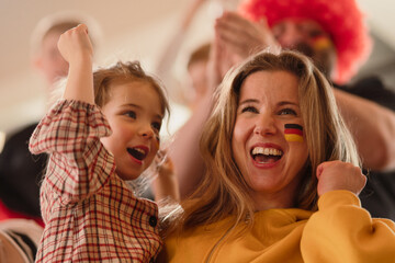 Excited football fans, mother with little daughter, supproting German national team in live soccer...