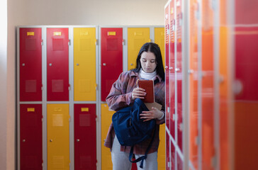 Sad teenage student standing in corridor near colorful lockers and packing book to backpack in campus hallway, back to school concept.
