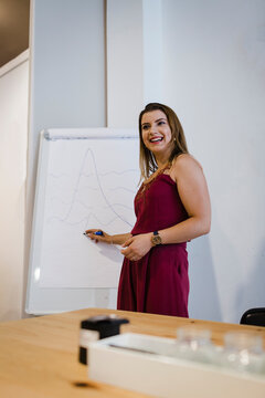 Smiling young businesswoman explaining diagram over flipchart in office meeting