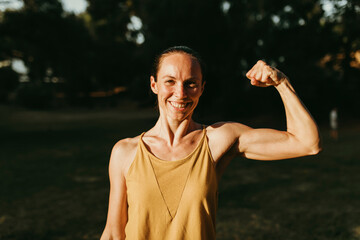 Happy woman flexing biceps in park