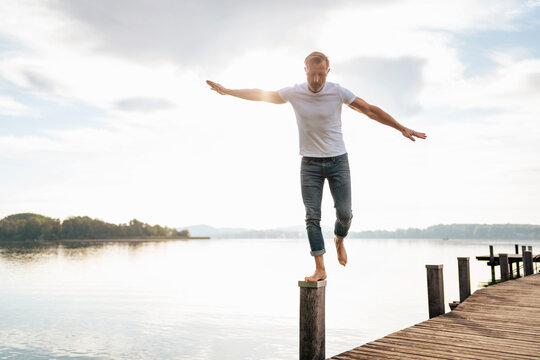 Mature man balancing on wooden post at pier by lake