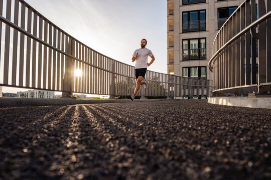 Young man in sports clothing running on footbridge