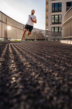 Young Man In Sports Clothing Jogging On Footbridge