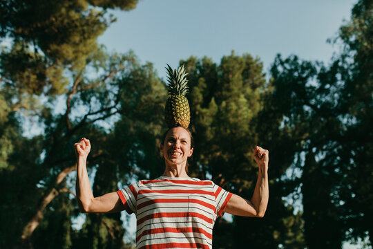Woman balancing pineapple on head and flexing muscles in park