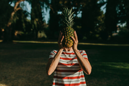 Woman covering face with pineapple in park
