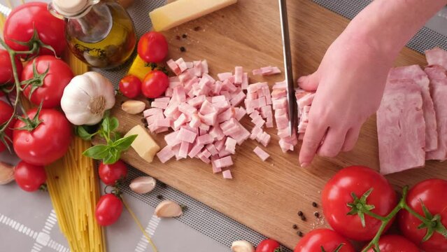 Making pasta carbonara - Slicing traditional pancetta bacon into pieces on a wooden cutting board with a knife