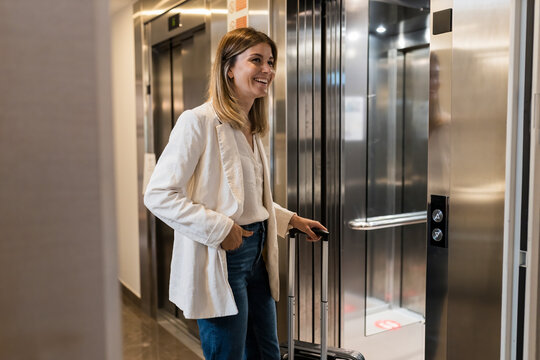 Happy businesswoman with suitcase walking into elevator