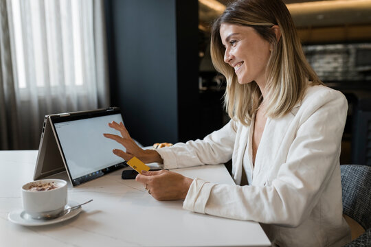 Happy businesswoman holding credit card doing online shopping through laptop at restaurant