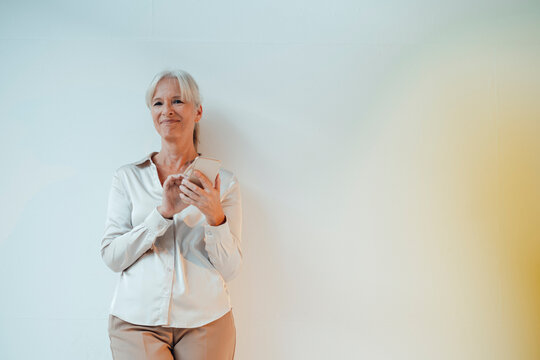 Smiling Businesswoman Holding Mobile Phone Standing Against White Background