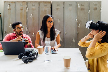 Businesswoman wearing VR goggles by colleagues in office