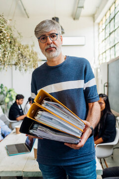 Mature businessman with eyeglasses holding files at workplace
