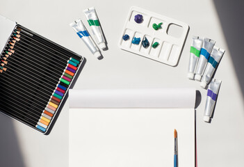Studio shot of art and craft equipment including colored pencils, blank drawing paper, oil paint tubes, artists palette and single paintbrush