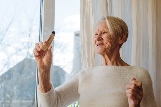 Happy senior woman with palo santo stick by window