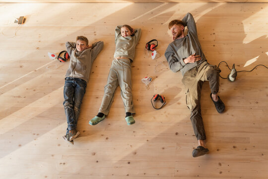 Father and kids have rest, lying after sanding the floor in an eco house. Top view, time together