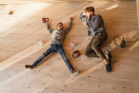Father and son have rest, lying after sanding the floor in an eco house. Top view, time together