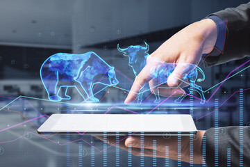  bulls and bears struggle. Equity market illustration. Close up of businessman hand holding and pointing at tablet with creative hologram and graph on blurry office interior background.