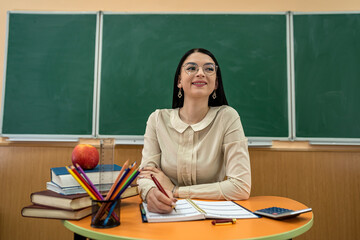 Woman teacher sits at a table with books and notebooks