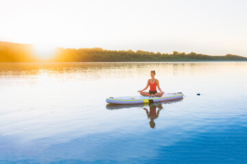 A woman relaxing herself doing yoga on a stand up paddle board. Summer heat cool down.