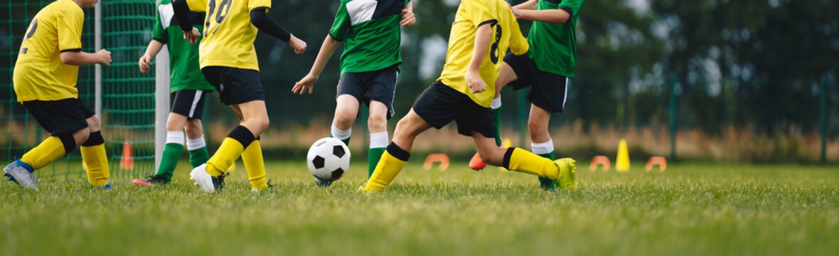 Kids play football on outdoor field. Children score a goal during a soccer game. Boys kicking ball. Running children in team jersey and cleats. School football club. Sports training for a young player