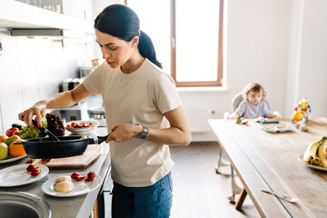 Smiling young mother cooking breakfast in the kitchen