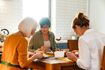 Mature three women laughing and eating cake during birthday lunch
