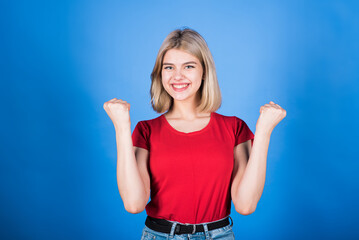 Young and attractive caucasian blonde girl in casual clothes clenching her fists and showing a winner gesture isolated on a blue studio background.