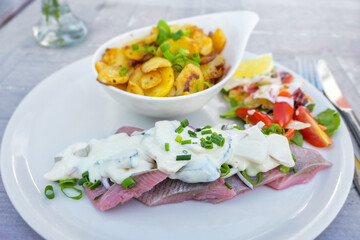 Matjes or soused herring, a mild salt fish with cream sauce containing onions, gherkins and apple, served with bratkartoffeln (German fried potatoes) and salad, selected focus